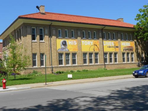A brick building with large banners reading "HISTORY LIVES HERE" and an astronaut graphic, surrounded by greenery.