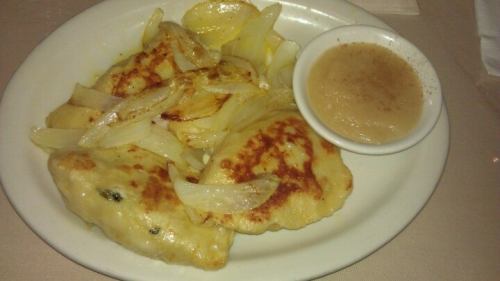 Plate of golden-brown pierogi topped with sautéed onions, served with a side of applesauce.