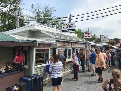 A busy bakery with a long line of customers outside, featuring signs for baked goods and a "What a Deal!" banner.