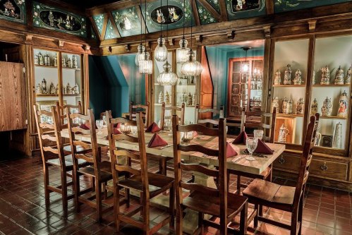 A rustic dining room with a long wooden table, wooden chairs, and glass display cabinets filled with decorative items.