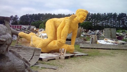 A large yellow sculpture of two figures in a playful pose, surrounded by various other sculptures in an outdoor setting.