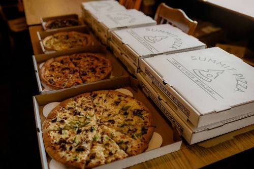 A table with several pizza boxes and various pizzas, including toppings like vegetables and meats.