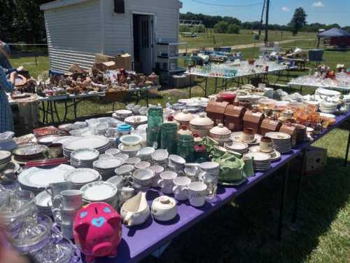 A vibrant outdoor market scene with tables filled with various dishes, glassware, and collectibles under a clear blue sky.