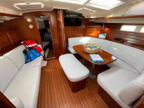 Interior of a sailboat featuring white seating, a wooden table, and natural light from overhead skylights.