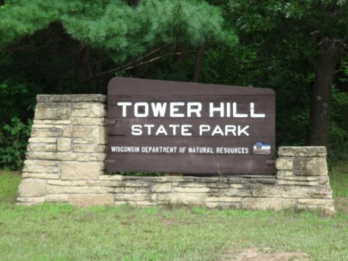 Sign for Tower Hill State Park, featuring stone base and greenery in the background.