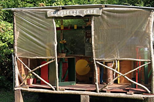 A rustic café structure with a sign reading "Sunbreeze Café," featuring wooden beams and a partially covered entrance.