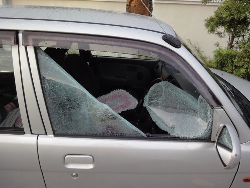 A silver car with a shattered window, showing broken glass and a partially visible interior.