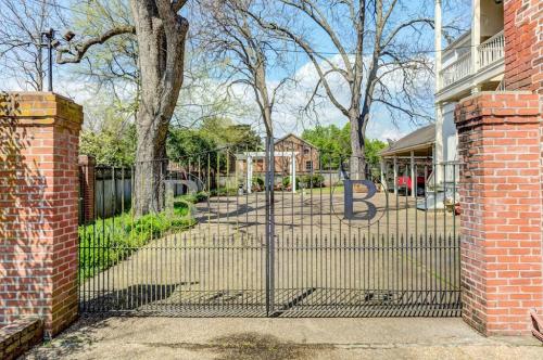 A wrought iron gate with two "B" letters opens to a tree-lined driveway and a brick building in the background.