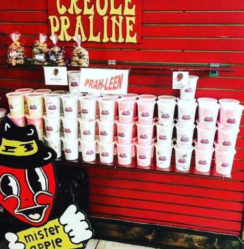 Display of colorful praline containers on a shelf, with a sign reading "Creole Praline" and a cartoon character.