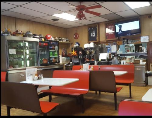 A cozy diner interior with red and brown seating, a drink cooler, and sports memorabilia on the walls.