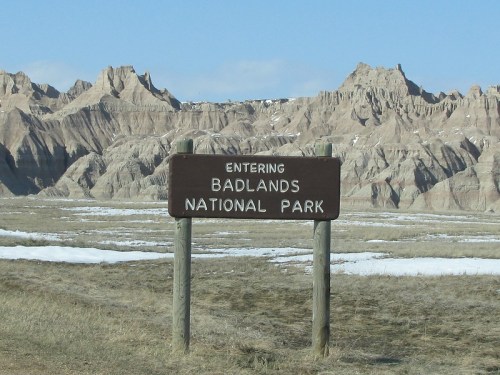 Sign marking the entrance to Badlands National Park, with rugged rock formations and a clear blue sky in the background.