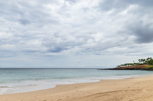 A serene beach scene with gentle waves, soft sand, and overcast skies in the background.