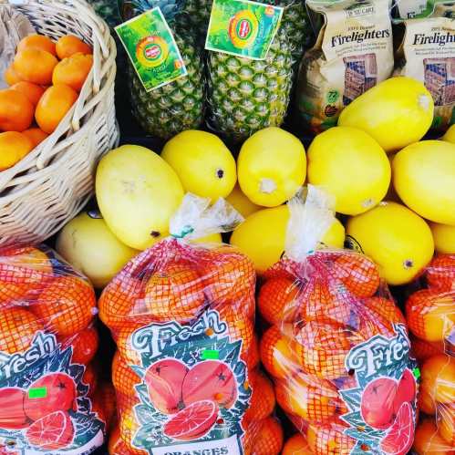 A vibrant display of fresh fruits, including oranges, lemons, pineapples, and a basket of small oranges.
