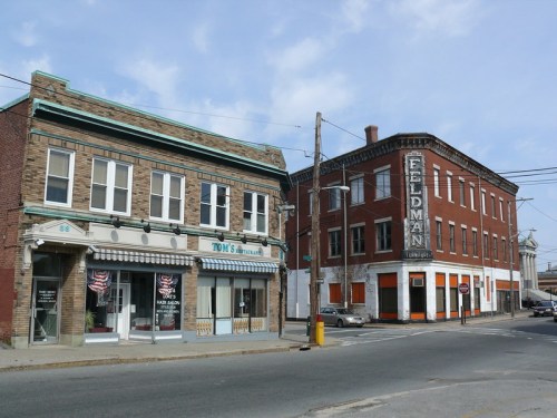 Two historic buildings on a street corner, one with a barber shop and the other labeled "Fieldman." Clear blue sky above.