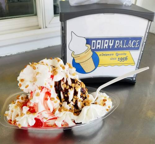 A delicious sundae topped with whipped cream, nuts, and syrup, next to a sign for Dairy Palace, established in 1956.