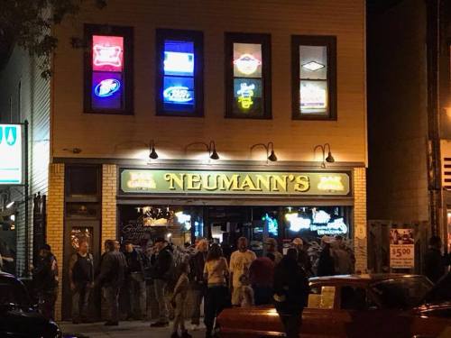 A lively bar scene at Neumann's, with neon signs and a crowd gathered outside on a bustling night.