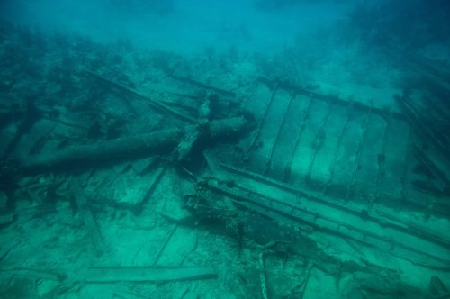 Underwater view of a shipwreck, with scattered debris and marine growth on the ocean floor.