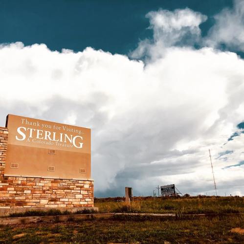 Sign welcoming visitors to Sterling, Colorado, with a backdrop of dramatic clouds and blue sky.