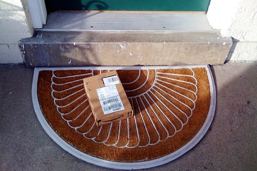 A small cardboard package sits on a decorative doormat at a front door.