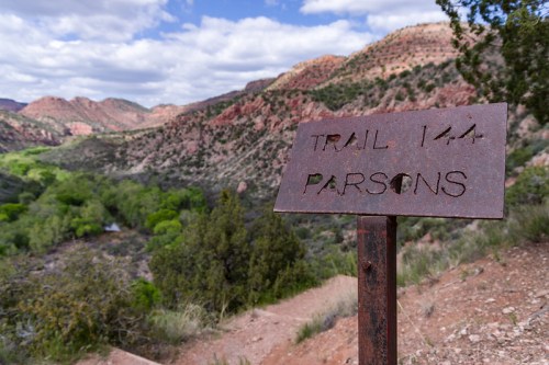 A weathered metal sign for Trail 144, labeled "Parsons," with a scenic mountainous landscape in the background.