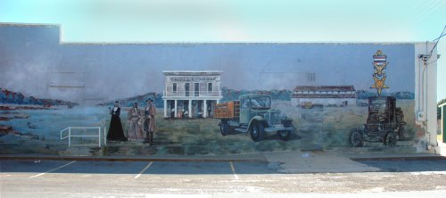 A mural depicting a historic scene with a building, vintage car, and figures in period clothing.