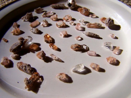 A white plate filled with various small crystals and mineral fragments, showcasing different shapes and colors.