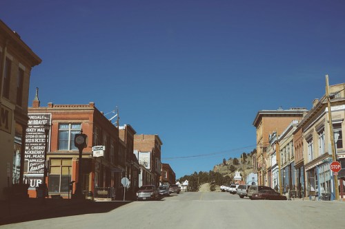 A quiet, historic street lined with vintage buildings and parked cars under a clear blue sky.