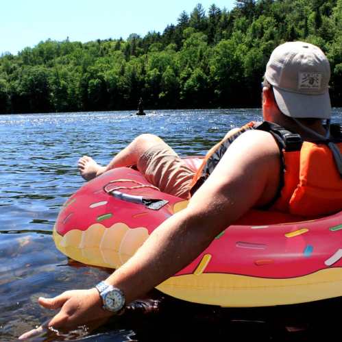 A person relaxes on a donut-shaped float in a lake, surrounded by trees and sunlight.