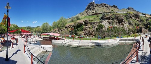 A panoramic view of a hot spring resort with pools, greenery, and rocky hills under a clear blue sky.