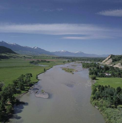 Aerial view of a winding river surrounded by lush greenery and mountains under a clear blue sky.