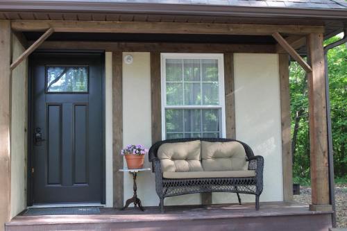 A cozy porch with a dark door, a wicker loveseat, and a potted plant on a small table, surrounded by greenery.