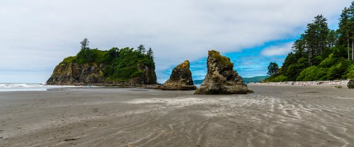 A scenic beach with rocky formations, lush greenery, and a cloudy sky in the background.