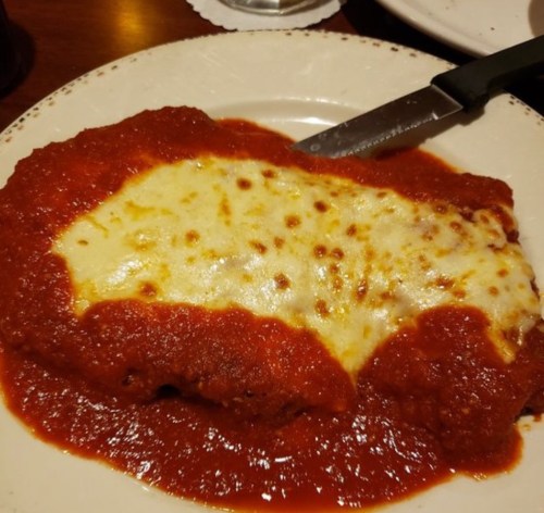 A plate of chicken parmesan topped with melted cheese and marinara sauce, served with a knife on the side.