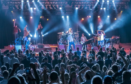 A lively concert scene with a band performing on stage, surrounded by an enthusiastic crowd under bright lights.