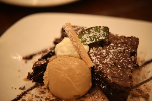 A rich chocolate brownie topped with ice cream, whipped cream, and a decorative wafer on a white plate.