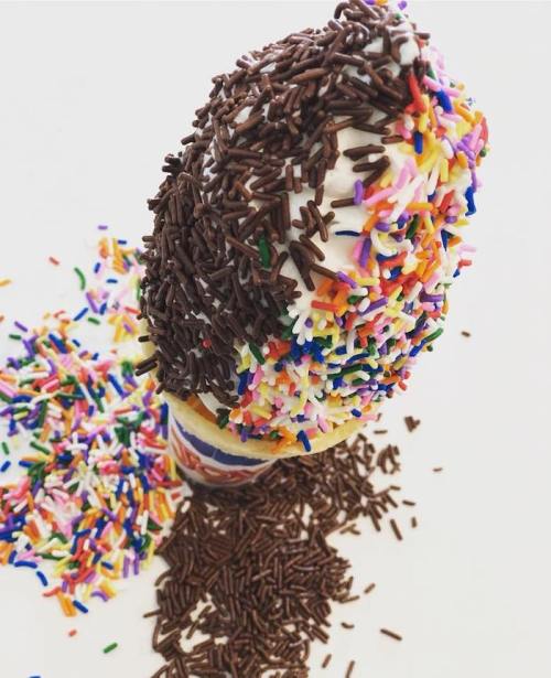 A colorful ice cream cone topped with chocolate and rainbow sprinkles, with extra sprinkles scattered around.