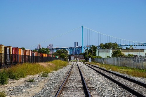 View of railway tracks leading towards a blue bridge, with freight containers and greenery on either side.
