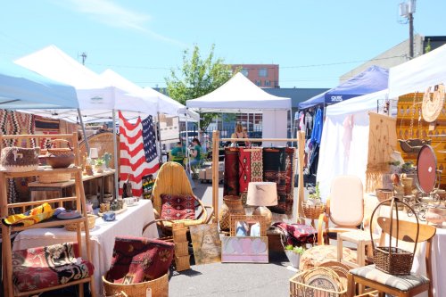 A vibrant outdoor market with tents displaying handmade crafts, textiles, and furniture under a clear blue sky.