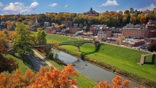 A scenic view of a town with autumn foliage, a river, and a bridge, showcasing vibrant fall colors and historic buildings.