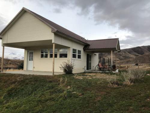A modern house with a porch, set against a backdrop of rolling hills and cloudy skies.