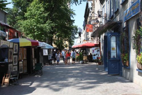 A charming street lined with art stalls and cafes, bustling with people under the shade of trees on a sunny day.
