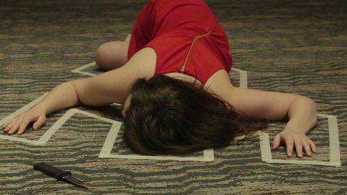 A woman in a red dress lies on the floor, outlined in tape, with a knife nearby.