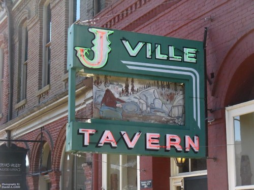 Sign for J Ville Tavern featuring a colorful design and a mural of a person playing drums.