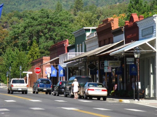 A quaint street lined with historic buildings, parked cars, and a person walking near a stop sign.