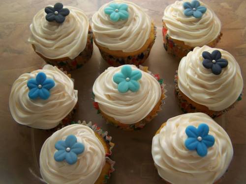 A tray of cupcakes with swirled frosting topped with blue and black flower decorations.