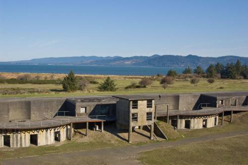 Abandoned concrete structures overlook a serene landscape with mountains and a body of water in the background.