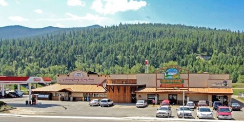 A scenic view of a gas station and a rustic store surrounded by green mountains under a clear blue sky.