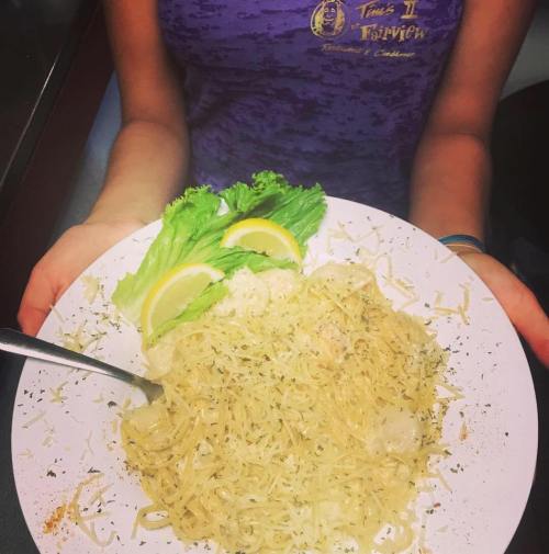 A person holding a plate of pasta with lemon slices and lettuce, garnished with herbs and cheese.