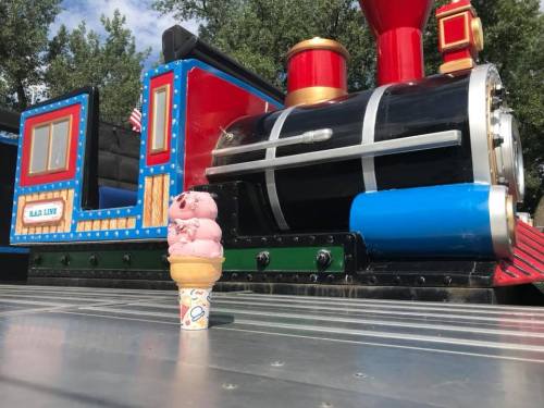 A colorful toy train beside a pink ice cream cone on a sunny day.