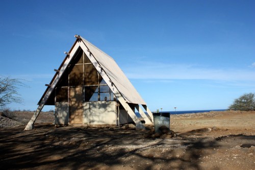A-frame structure with large windows, set against a clear blue sky and coastal landscape.